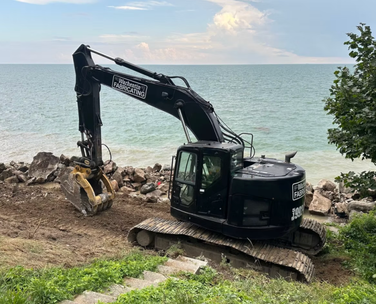 Hybrid steel and armor stone breakwalls reduce direct wave impact by dissipating energy through layered stone before it reaches the structural wall. This helps limit cracking, scour, and long term structural fatigue. Photo Credit: Warkentin Fabricating