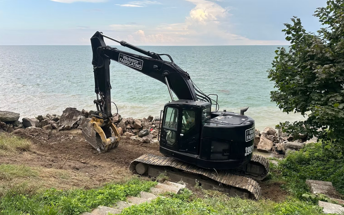 Hybrid steel and armor stone breakwalls reduce direct wave impact by dissipating energy through layered stone before it reaches the structural wall. This helps limit cracking, scour, and long term structural fatigue. Photo Credit: Warkentin Fabricating