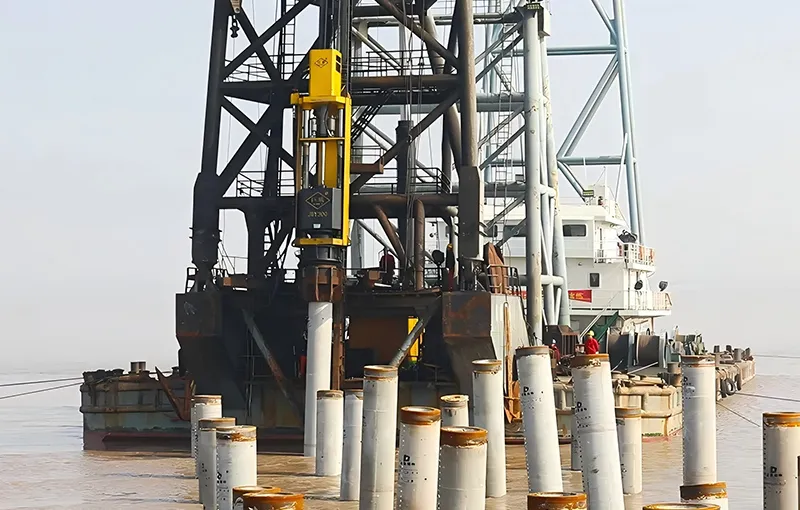 Pile hammers install deep foundations by delivering repeated impact energy that pushes piles into the ground. The amount of energy delivered affects penetration speed and final pile capacity. Photo Credit: JUWEl Machinery